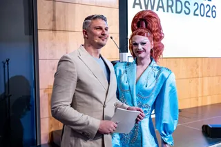 Die Moderator*innen der Queermentor Role Model Awards Pavlo Stroblja (links) und Rachel Intervention (rechts) stehen zusammen auf der Bühne. und lächeln in die Kamera.